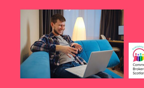 A man sits on a sofa taking part in a video call on his laptop